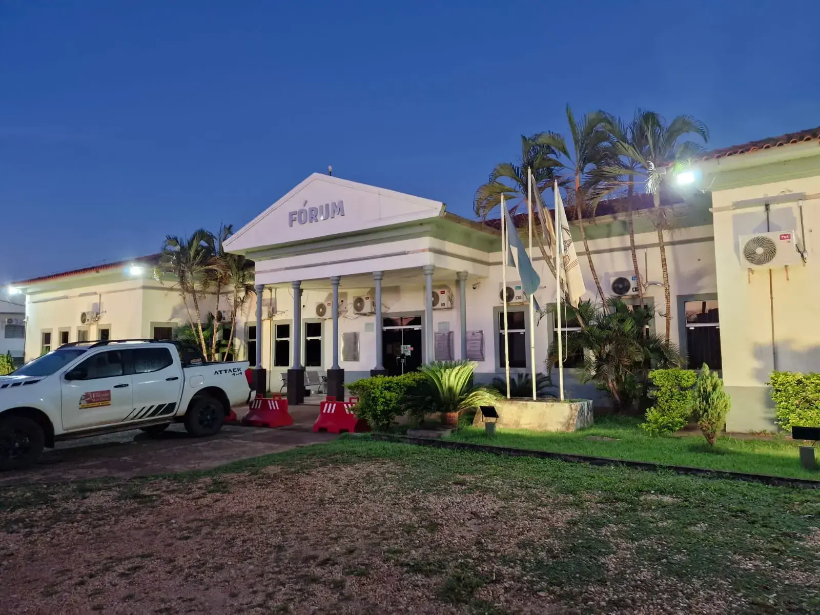 Fachada do Fórum de Aripuanã sob o céu azul ao anoitecer. O prédio tem estilo neoclássico, com cinco colunas em seu pórtico central. Palmeiras plantadas nas laterais desse pórtico de entrada, em meio ao jardim. Há uma caminhonete do Poder Judiciário estacionada em frente.