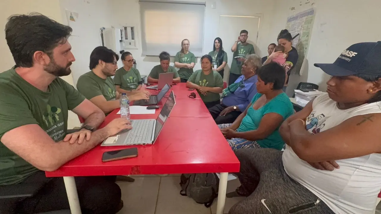 Foto colorida que mostra diversas pessoas em volta de uma mesa em uma sala. Trata-se de uma audiência de instrução e julgamento ocorrida durante mutirão na aldeia indígena Campinas. O juiz, o promotor, as advogadas e demais servidores usam camiseta verde do projeto.