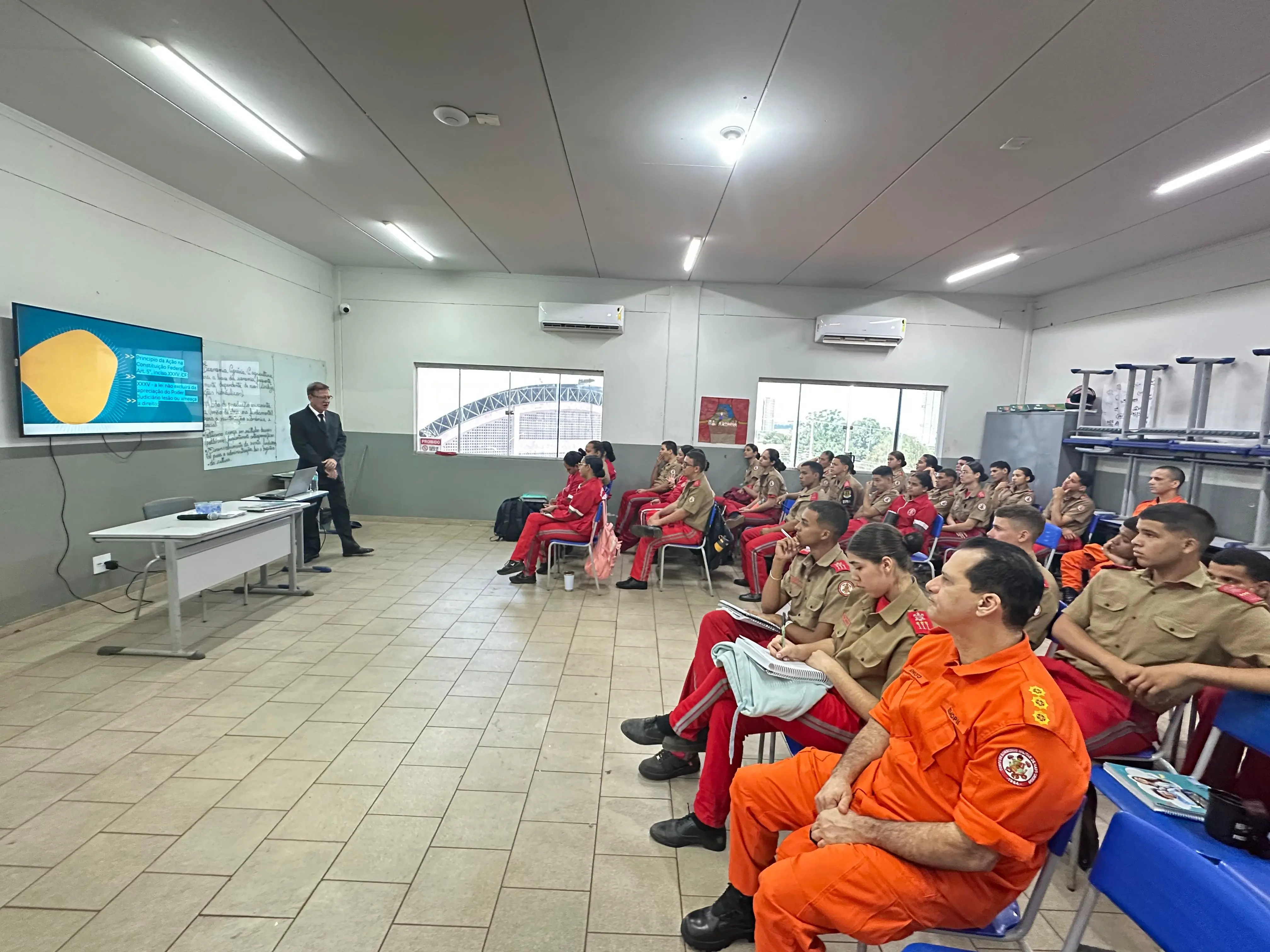 Juiz conversa com turma de jovens da Escola Militar Dom Pedro II, em Rondonópolis. A plateia, de fardas vermelhas e beges, ouve atenta à palestra sobre direitos humanos e acesso à justiça.