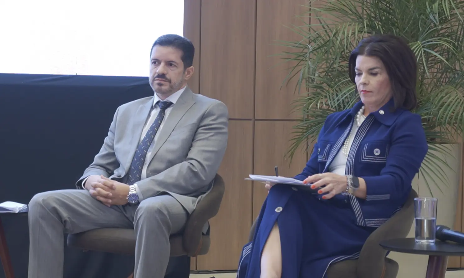 Juiz Jamilson Haddad e Jaqueline Cherulli sentados em poltronas, enquanto participam de painel do congresso. O juiz é um homem branco, de cabelos e olhos castanhos, barba grisalha, usando terno cinza. A juíza é uma mulher branca, de cabelo castanho com corte chanel, usando conjunto de saia e blazer