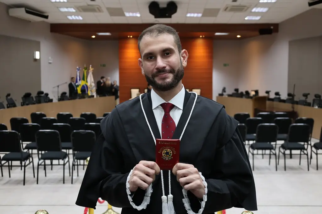 Foto do juiz Magno Batista exibindo sua carteira funcional. ele é um homem branco, alto, de barba, usando toga. Ele está no Plenário 1 do Tribunal de Justiça de Mato Grosso.