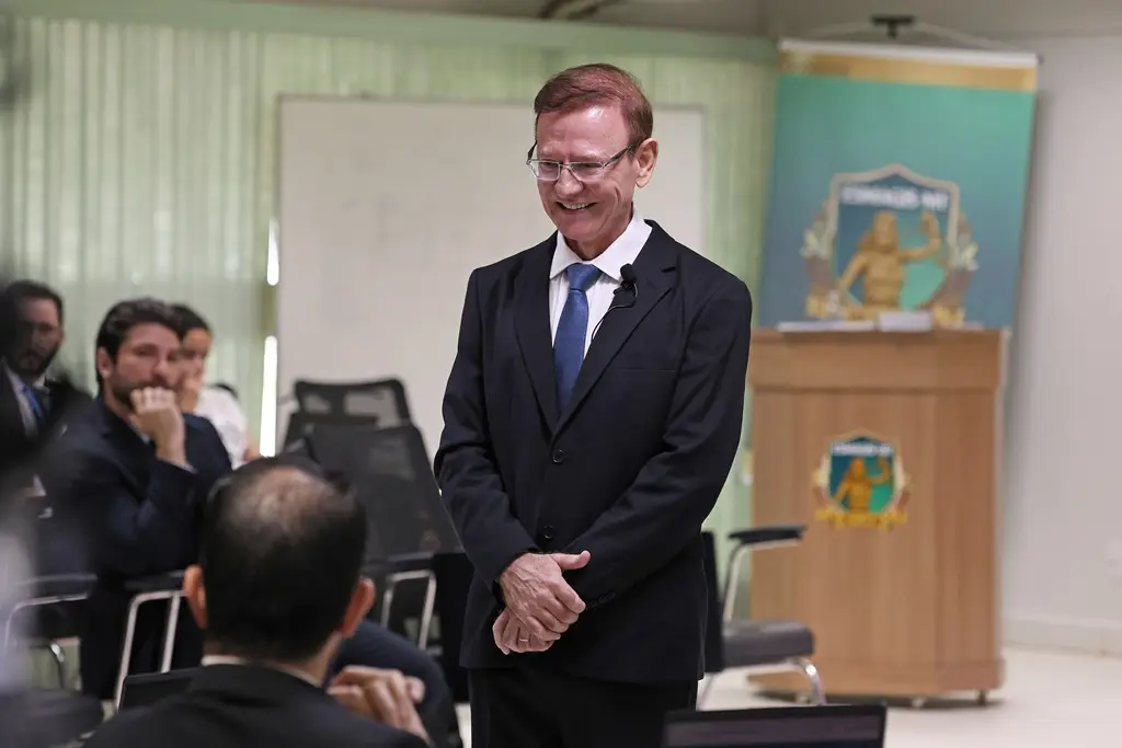 Foto horizontal em plano médio, que mostra o juiz Wanderlei Reis durante sua aula, em pé no meio da sala de aula, olhando para um aluno, que está sentado. Os alunos aparecem sentados em volta do professor. 