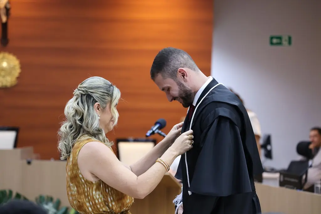 foto horizontal que mostra o juiz Magno Batista de frente para uma familiar que lhe auxilia a vestir a toga, durante sessão de posse no TJMT.