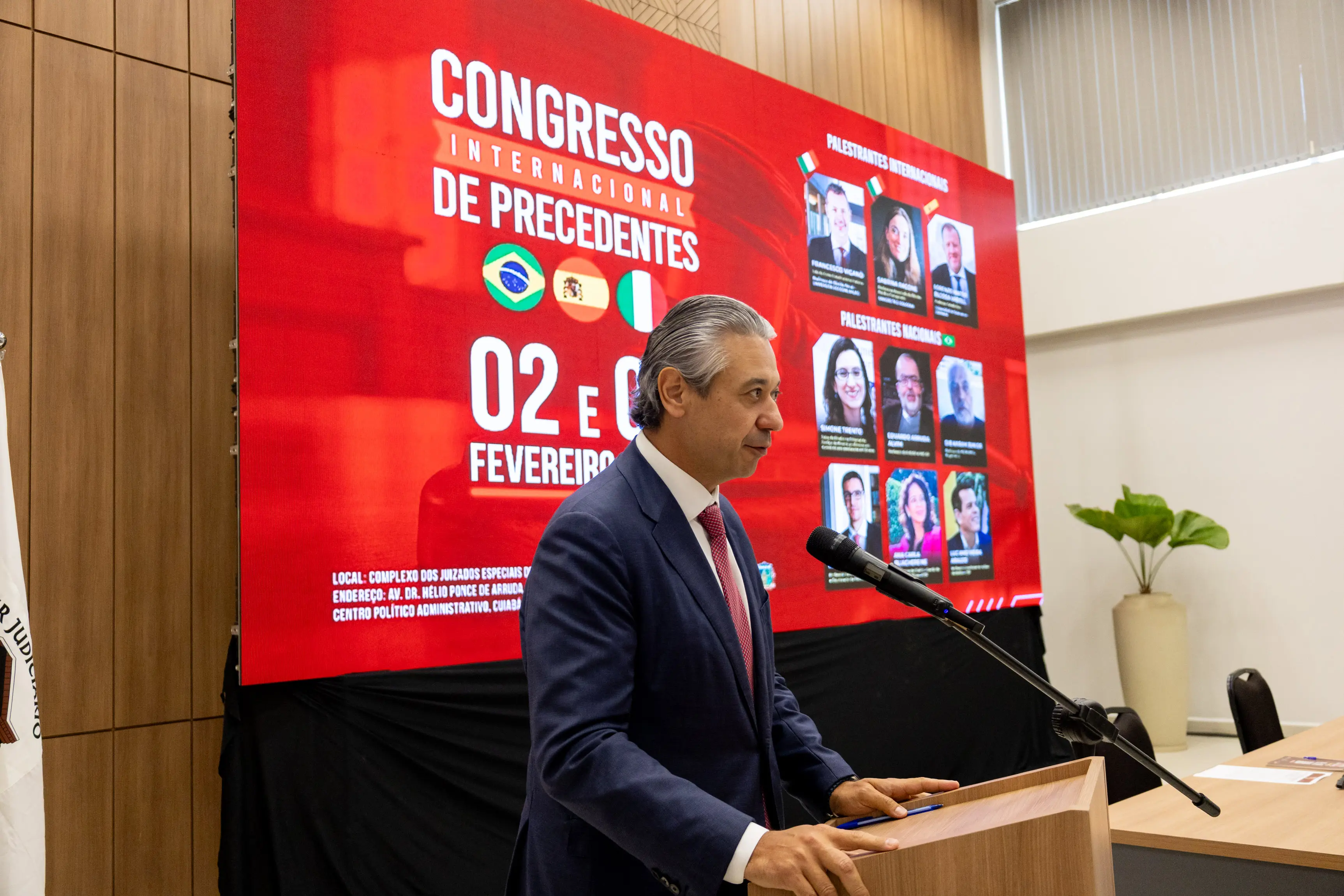 Um homem de cabelo grisalho e terno azul discursa em um púlpito. Ao fundo, um grande telão vermelho exibe "CONGRESSO INTERNACIONAL DE PRECEDENTES" e fotos de palestrantes nacionais e internacionais.