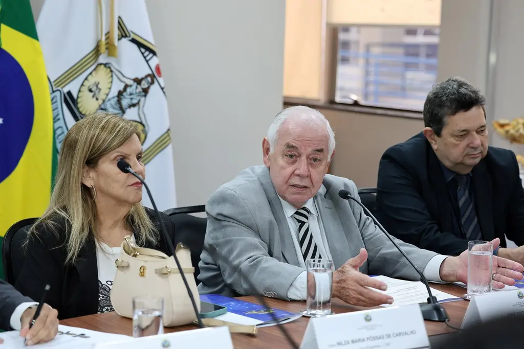 Foto horizontal que mostra o presidente e a vice-presidente do TJMT e o corregedor-geral da Justiça sentados um ao lado do outro, em volta de uma mesa. O presidente, desembargador José Zuquim aparece ao centro, falando ao microfone. Ele é um senhor branco, de cabelos brancos, olhos claros.