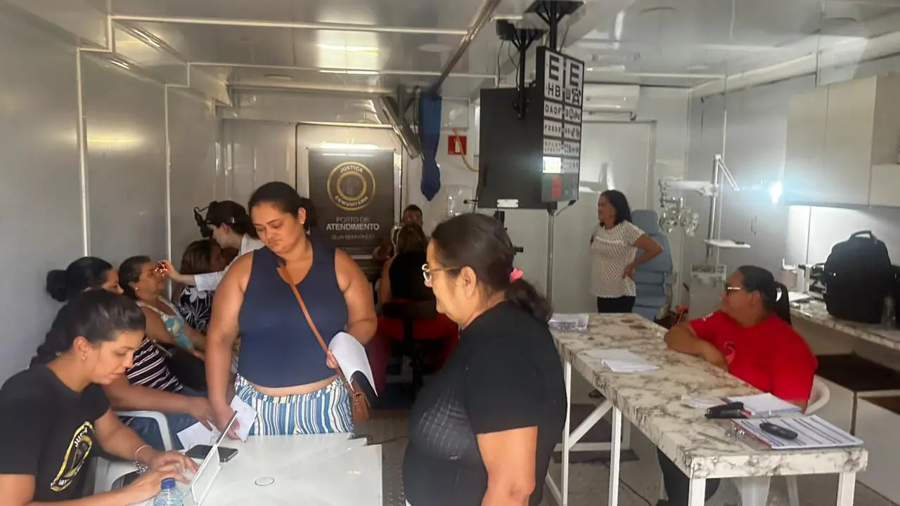 Interior da unidade móvel mostra atendimento ao público. Cidadãos aguardam em cadeiras enquanto funcionários realizam atendimentos em balcões. Ambiente climatizado e organizado, com sinalização institucional do Poder Judiciário visível ao fundo.