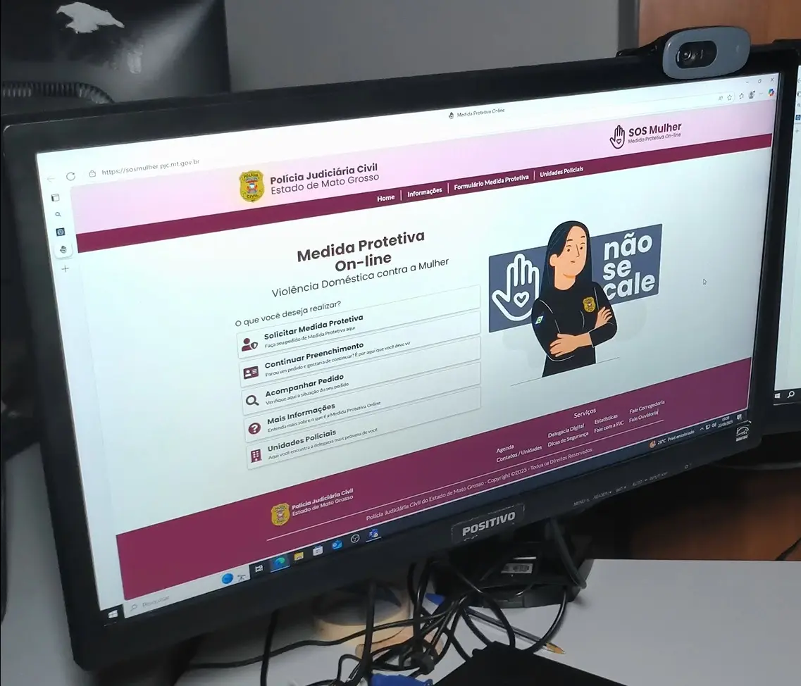 Foto horizontal que mostra o monitor de um computador ligado. Na tela, aparece o site da Polícia Civil de Mato Grosso, na página de solicitação de medida protetiva on-line.