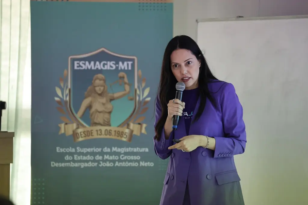 Foto horizontal da juíza Joseane Antunes, coordenadora do laboratório de inovação do TJMT, falando ao microfone, em uma sala de aula da Escola da Magistratura. Ela é uma mulher branca, de olhos e cabelos pretos, usando blazer roxo.