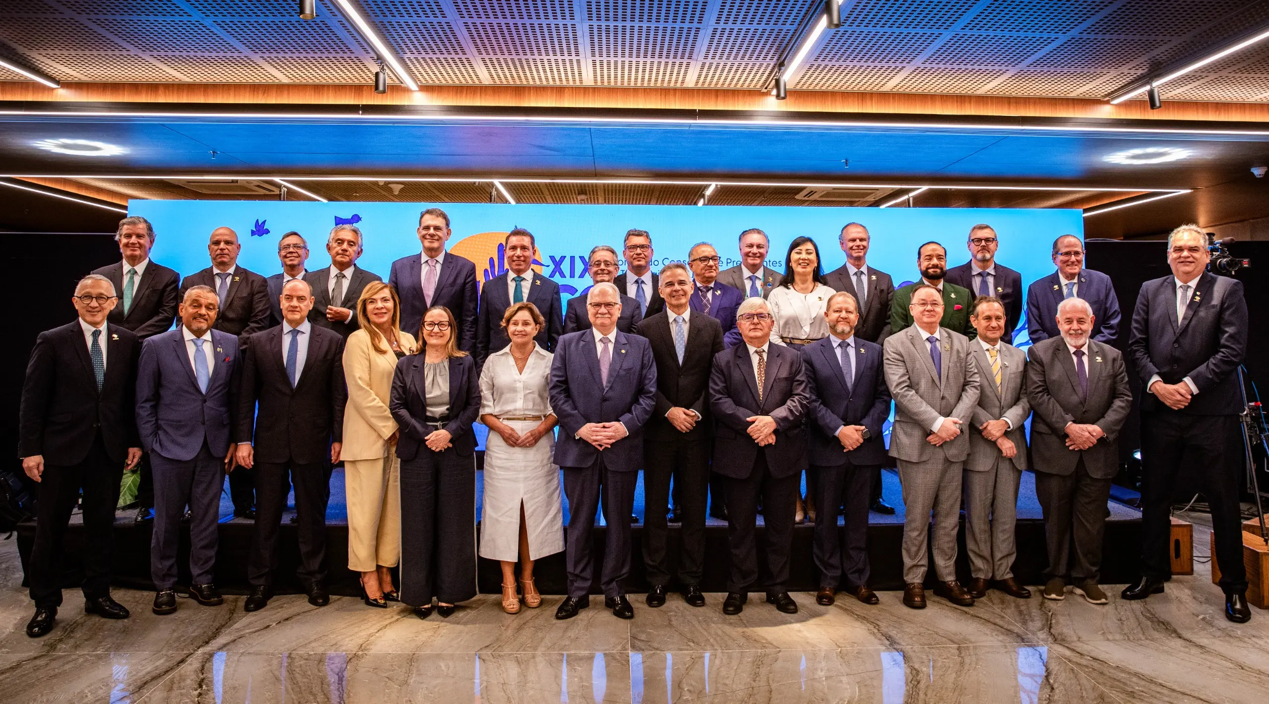 Autoridades do Judiciário posam para foto oficial no encerramento do XIX Consepre. Em dois níveis, magistrados e presidentes de tribunais estão alinhados diante de painel azul do evento, em ambiente moderno e iluminado.