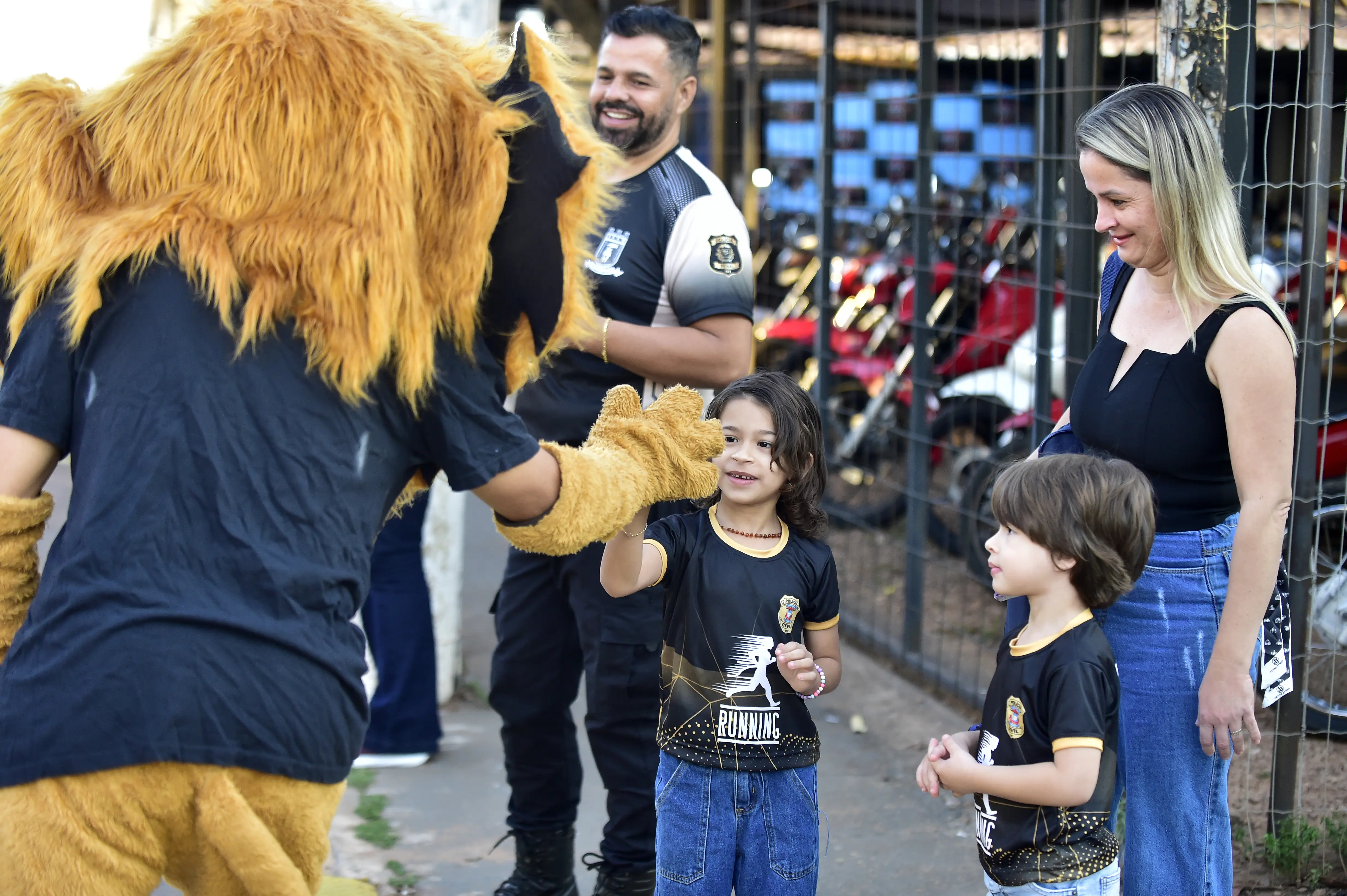 Um mascote de leão cumprimenta uma criança com um "high-five" em frente a uma família sorridente durante o evento.
