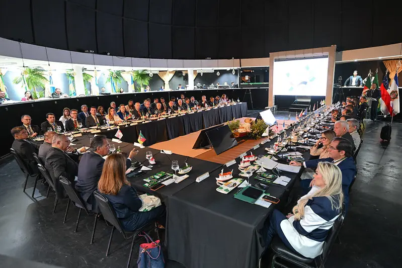 Foto em plano aberto que mostra os representantes das Ouvidorias Judiciárias reunidos em uma grande mesa em formato de U, em um grande salão. 