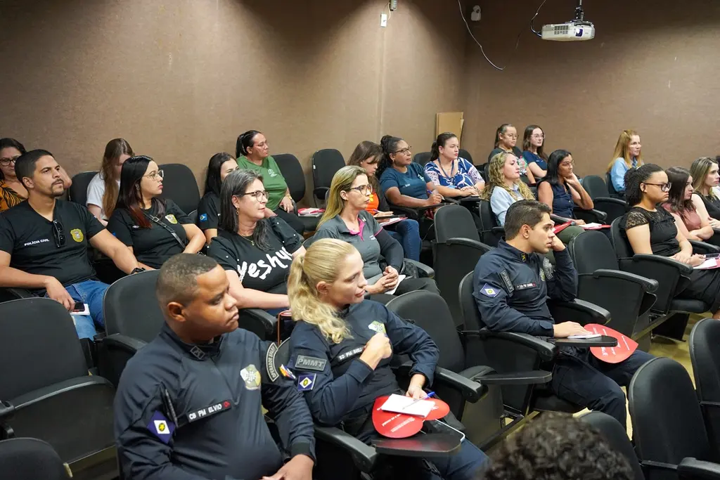 Diversas pessoas, várias com uniformes de órgãos públicos, sentados em um auditório, participando de uma palestra.