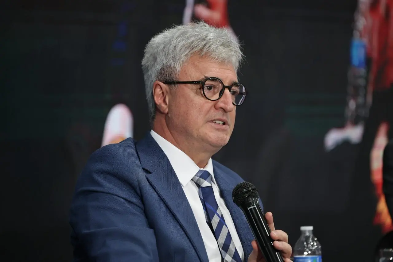Desembargador Roberto Bacellar fala ao microfone, durante palestra. Ele é um senhor branco, de cabelos brancos, olhos escuros, usando camisa branca, paletó azul, gravata xadrez azul e cinza e óculos de grau.