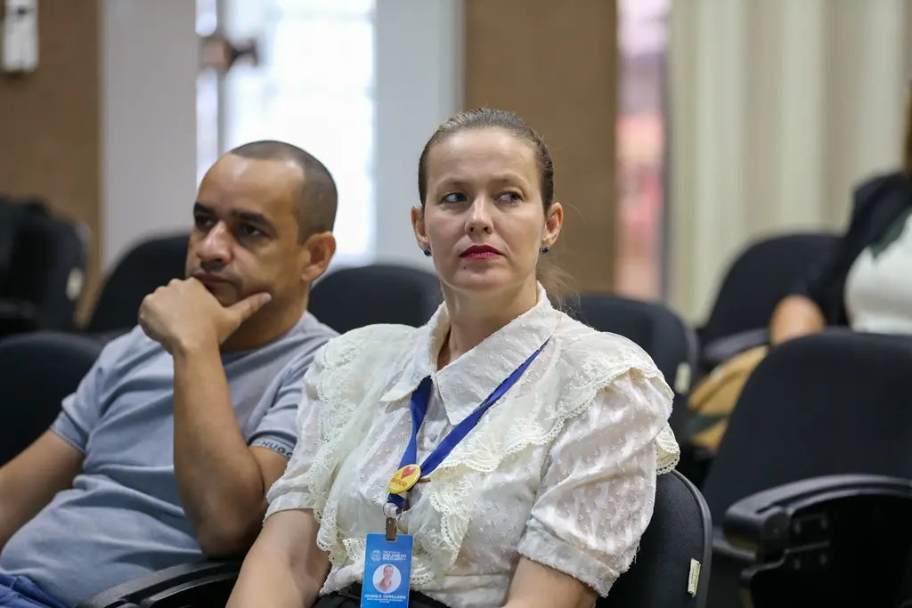Secretária de Educação e Cultura de São José do Rio Claro sentada em um auditório. Ela é uma mulher branca, loira, usando camisa branca.