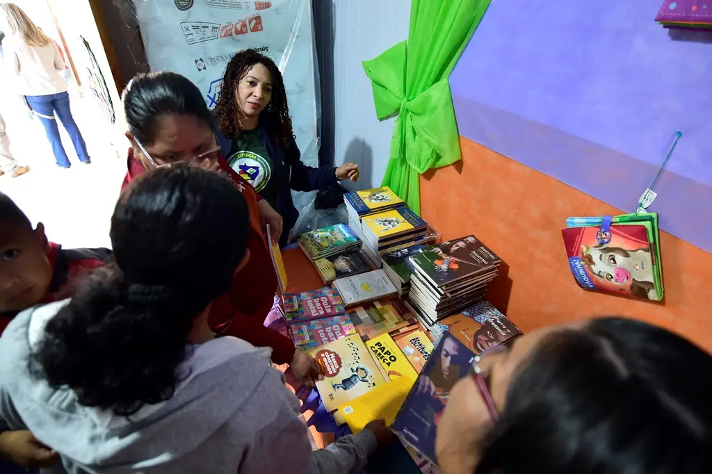 Foto tirada de cima, mostrando várias pessoas em volta de uma mesa cheia de livros para doação, em uma sala de aula.