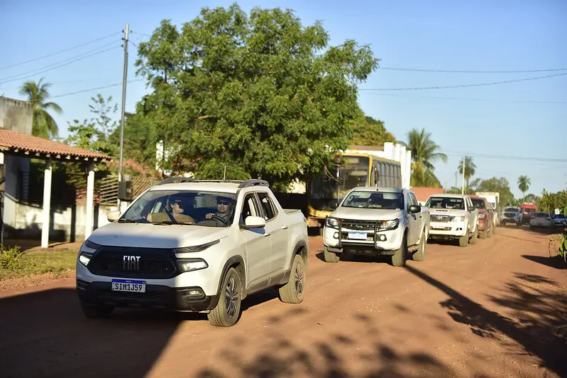 Foto que mostra o comboio da expedição Justiça Sem Fronteiras chegando ao distrito de Vila Picada, numa rua de chão.