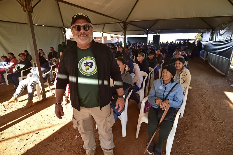 Foto que mostra o juiz José Antônio Bezerra Filho posando para a foto, sorrindo e em pé, em frente a uma multidão que aguarda sentada embaixo de uma tenda. O juiz usa camiseta do Justiça Sem Fronteiras.