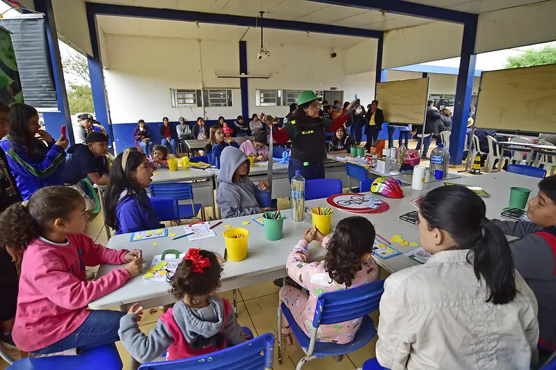 Foto em plano aberto que mostra o pátio da Escola Estadual 12 de Outubro repleto de crianças participando de oficinas lúdicas do Detran.