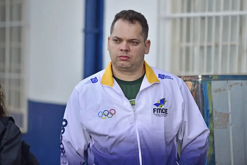 Homem branco, de olhos claros e cabelo castanho claro, usando moletom esportivo. Ele aparece da cintura pra cima na foto e está olhando para o lado.