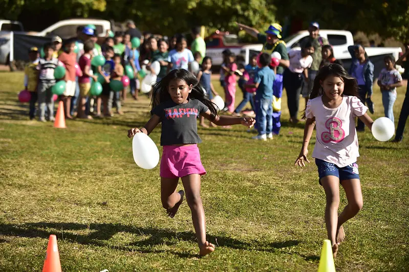 Foto que mostra crianças correndo e participando de uma gincana no gramado da Escola 11 de Agosto.