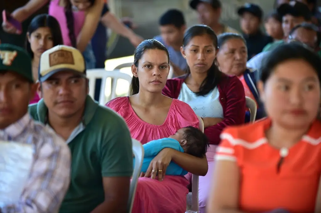 Várias pessoas sentadas, aguardando atendimento no mutirão Justiça Sem Fronteiras. Em primeiro plano, no centro, está uma mulher vestida com um vestido rosa, segurando um bebê no colo. Ela olha para a foto. 