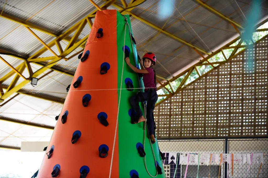 Uma menina sobre na torre de escalada inflável do Corpo de Bombeiros, em uma quadra esportiva.