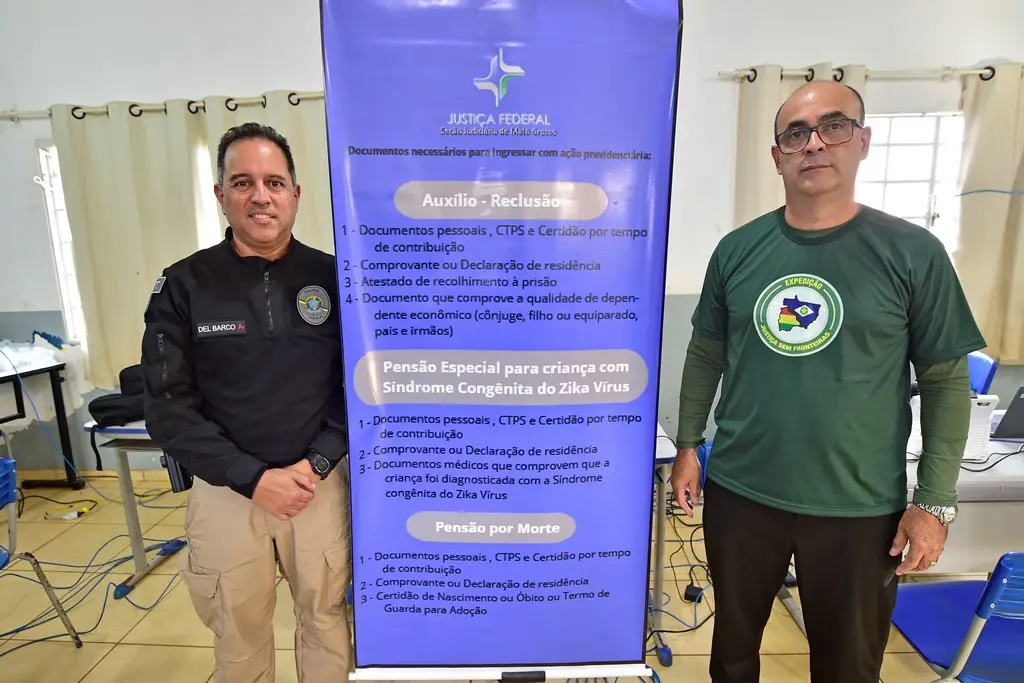 Foto que mostra dois servidores da Justiça Federal posando ao lado de um banner que informa os serviços oferecidos no mutirão.