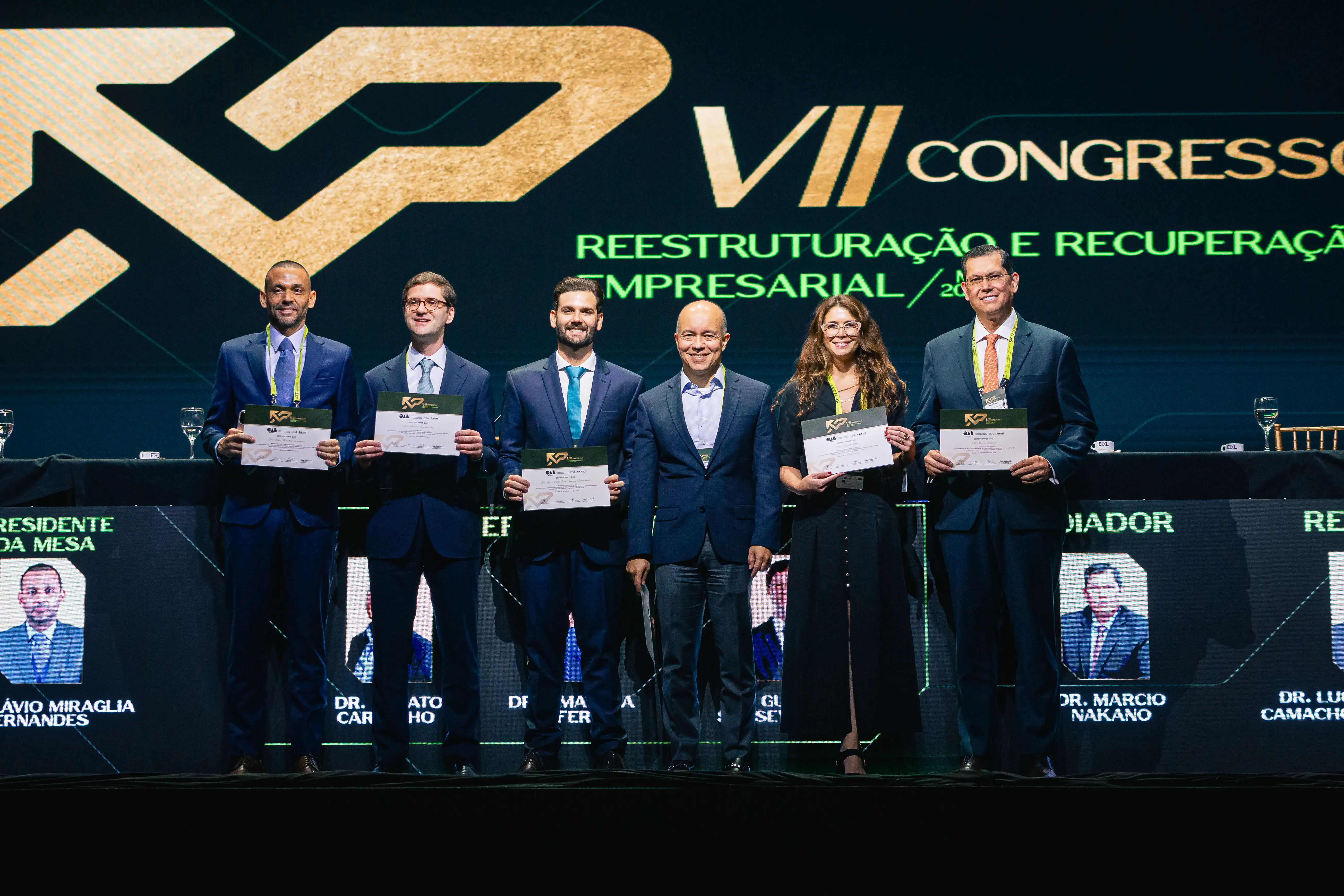 Foto que mostra o juiz Flávio Miraglia ao lado de advogados e empresários posando para a foto no 7º congresso de Reestruturação e Recuperação Empresarial. Eles estão em pé, segurando certificados de participação no evento.