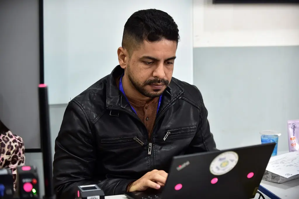 Servidor da Politec trabalhando no computador. Ele é um homem negro, de cabelo preto, usando jaqueta de couro preta.