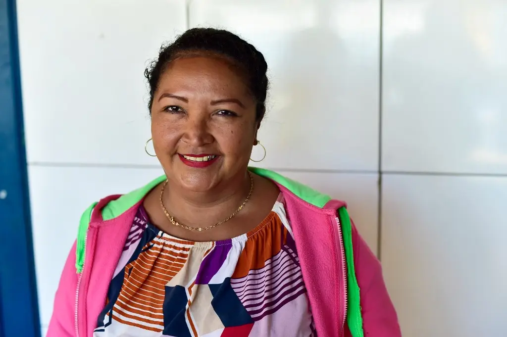 Mulher posa sorrindo para a foto. Ela fez penteado no mutirão Justiça Sem Fronteiras. Ela é negra, tem cabelos e olhos pretos, usando blusa e moletom coloridos e brincos de argola.
