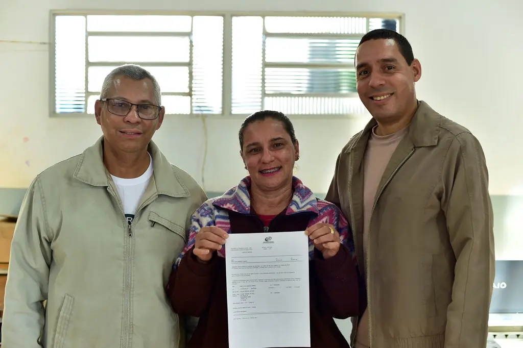 Servidores do INSS e mulher atendida por eles posam para a foto sorrindo. A mulher, no centro, mostra um documento.