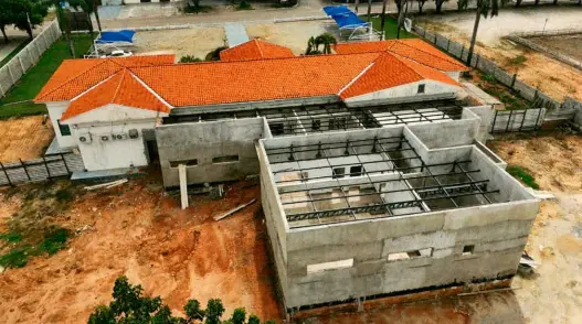 Vista aérea das obras de ampliação do Fórum de Paranaíta. Em destaque, uma nova estrutura de concreto com vigas de aço expostas, integrada ao prédio original de telhado cerâmico laranja.