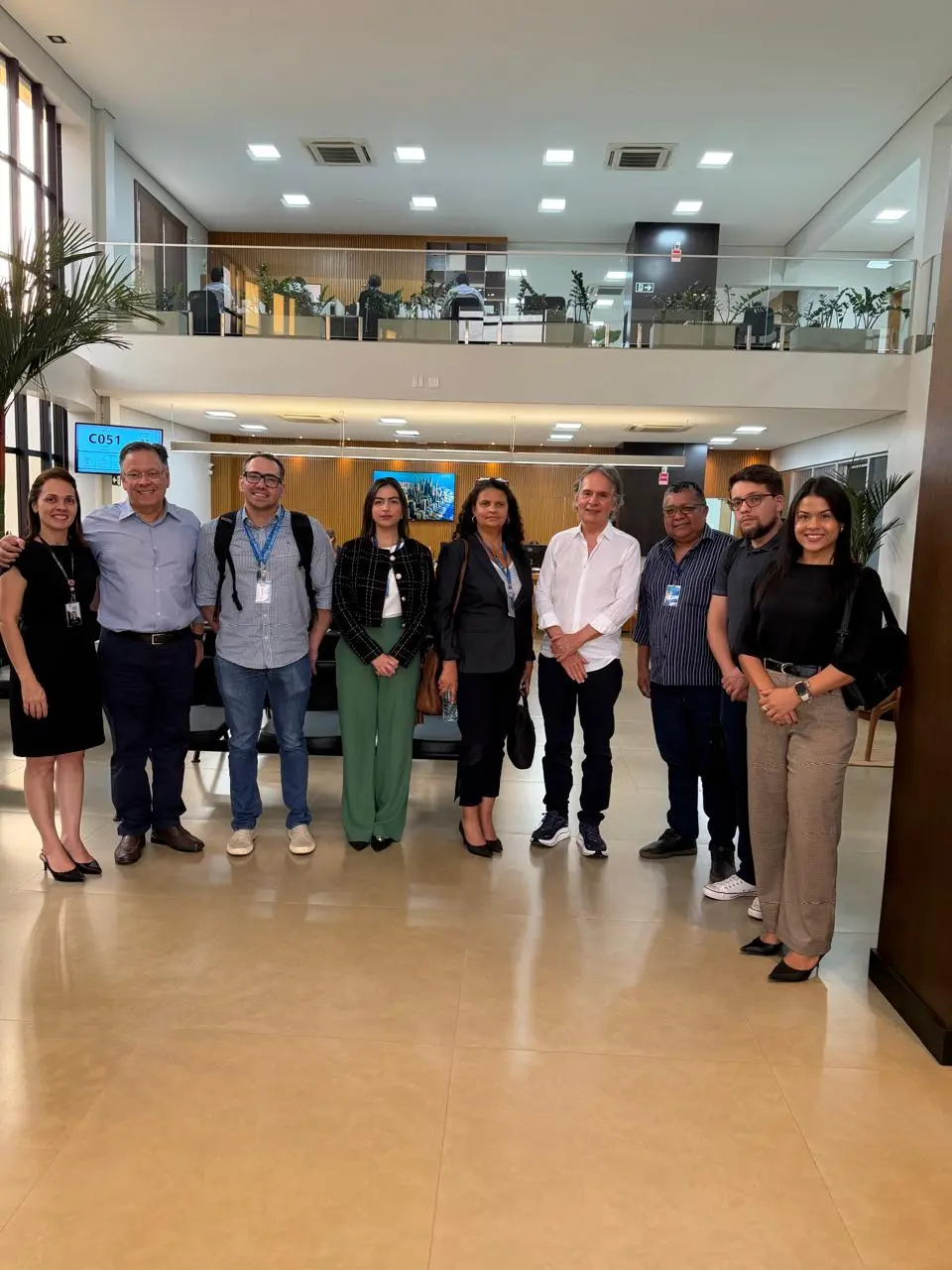 A assessora Aline Bottezel da Rosa, diretora do Departamento Foro Extrajudicial (DFE), Nilcemeire Vilela e equipes do TJMT e cartório do 1º Ofício de Sorriso posam lado a lado em ambiente interno, com mesas, cadeiras e estações de trabalho ao fundo. O espaço tem dois pavimentos, ligados visualmente