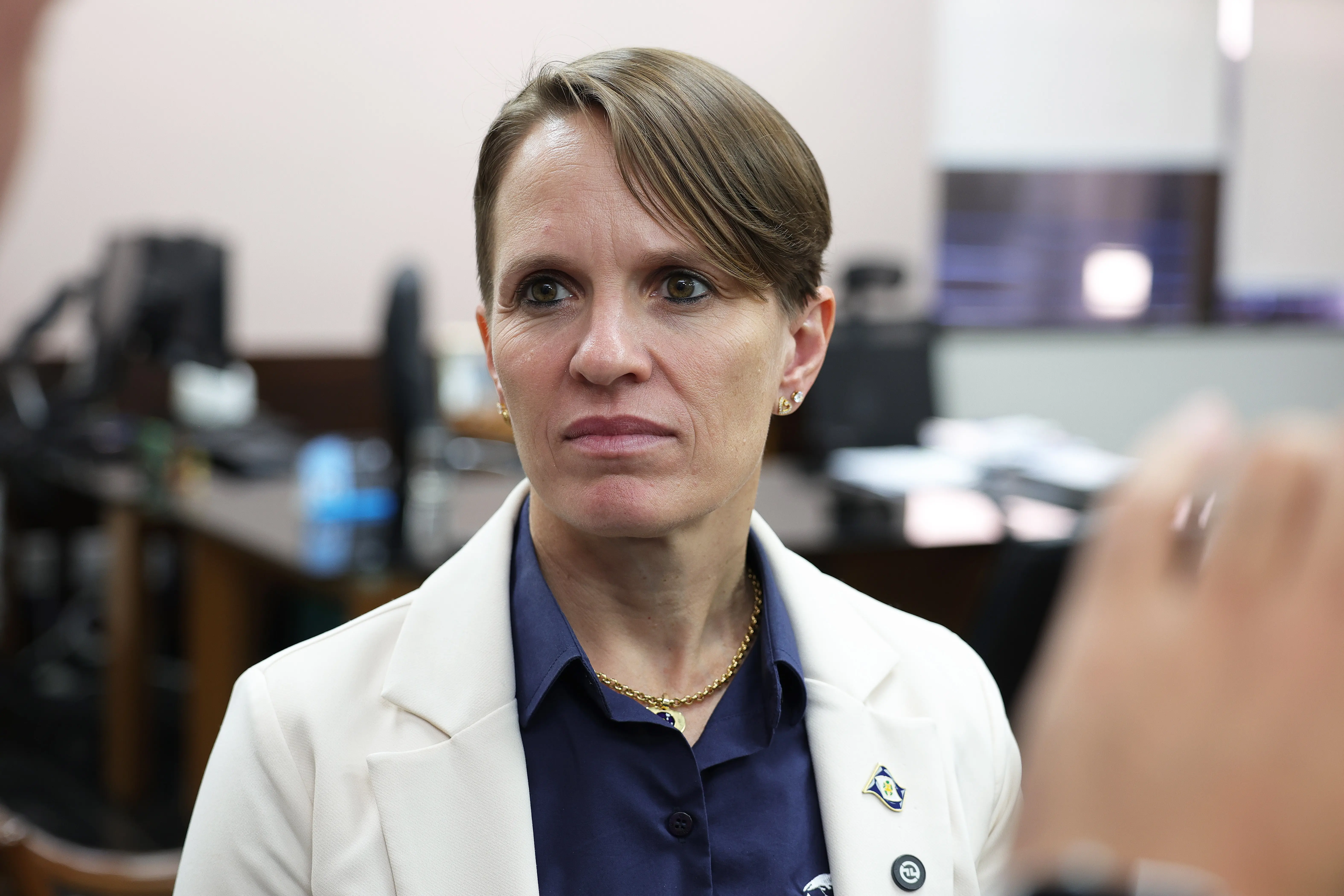 secretária de Segurança Pública, coronel da reserva Susane Tamanho tem de cabelo curto e loiro, veste um blazer branco sobre uma camisa azul marinho e um colar dourado, olha ligeiramente para a esquerda.