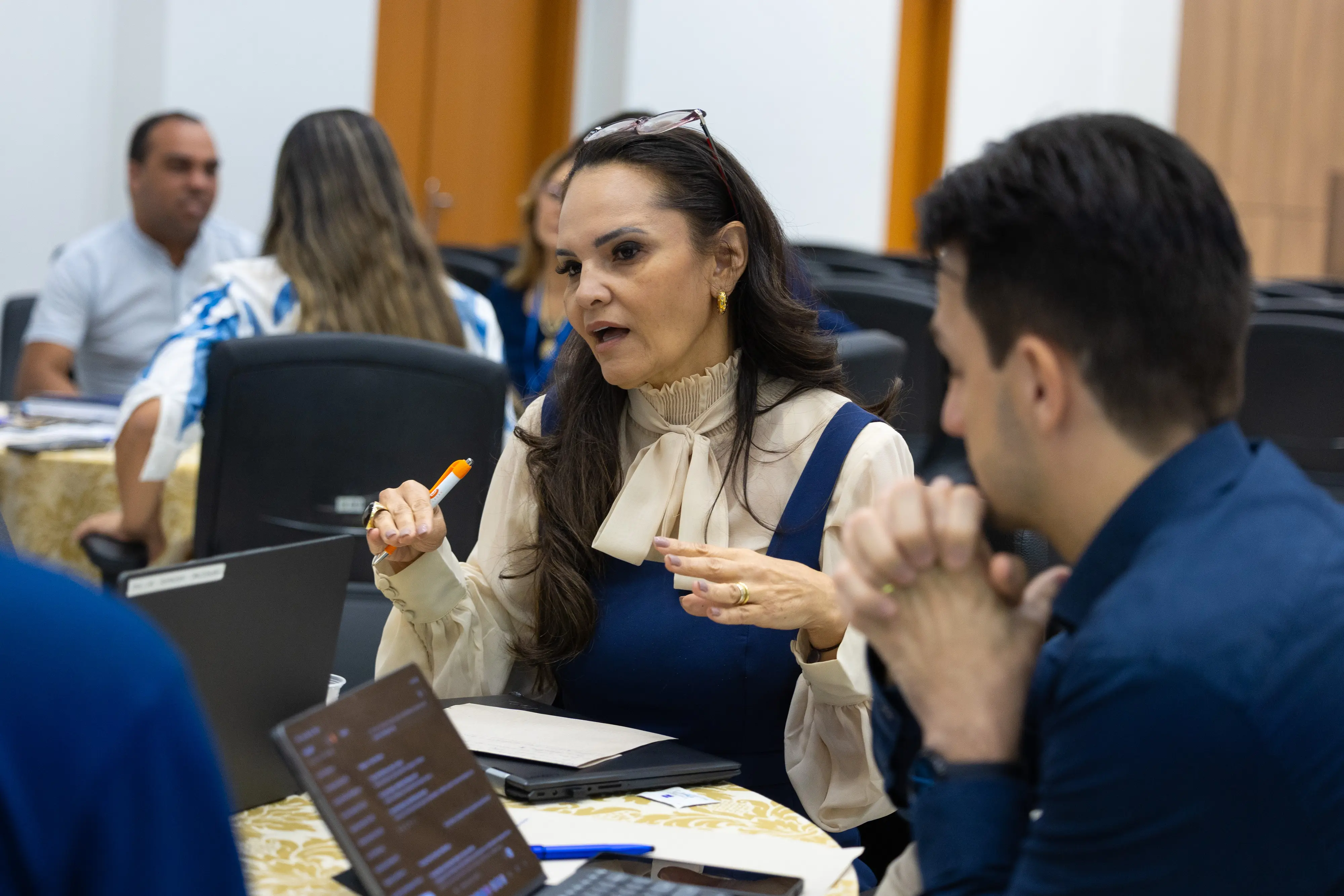 Mulher gesticula enquanto conversa em roda de discussão. Participantes observam atentos durante a atividade.