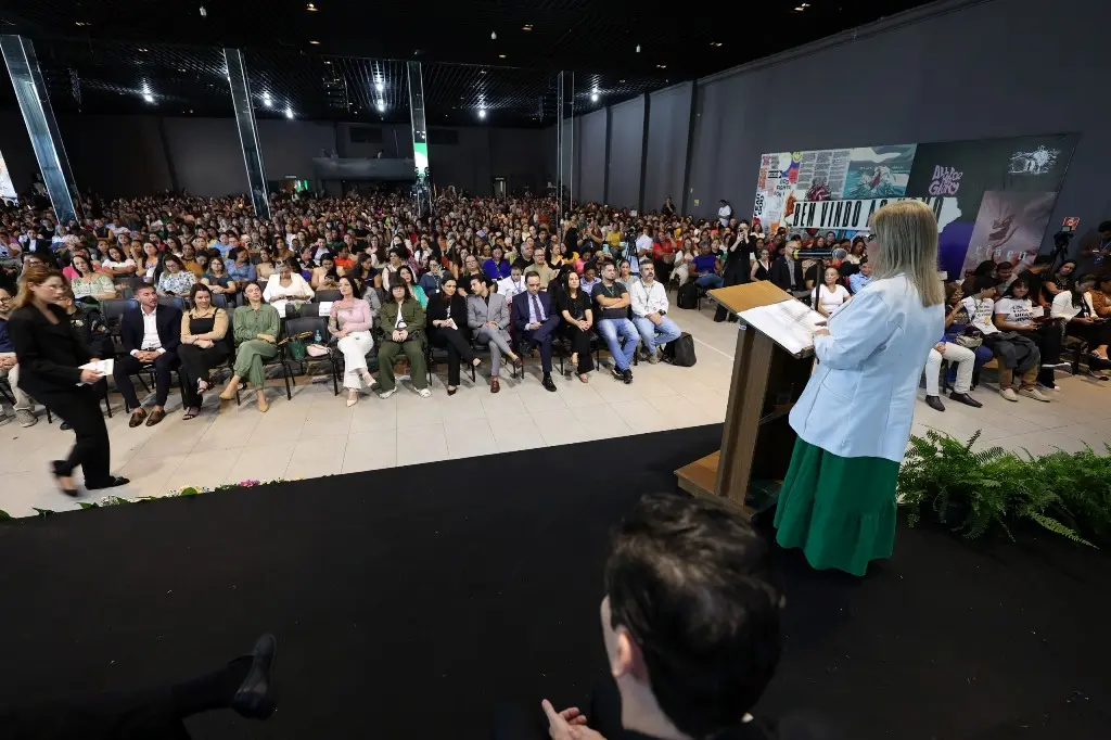 Foto horizontal em plano aberto que mostra o interior da Igreja Lagoinha lotado de pessoas sentadas, participando do evento TJMT Inclusivo. No palco, de costas para a foto, está a desembargadora Nilza Maria falando no púlpito.