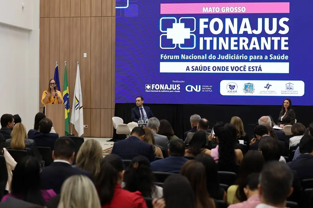 Foto horizontal que mostra o auditório lotado de pessoas assistindo palestra no Fonajus Itinerante. À frente, há um enorme telão com a logomarca do evento e a diretora da ANS profere palestra.
