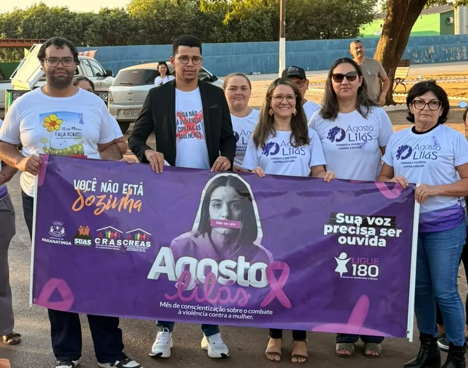 A equipe, de sete pessoas, do Fórum de Paranatinga posa para foto, segurando um grande banner roxo da campanha Agosto Lilás, com mensagens de apoio às mulheres e combate à violência, todas reunidas em um ambiente externo.