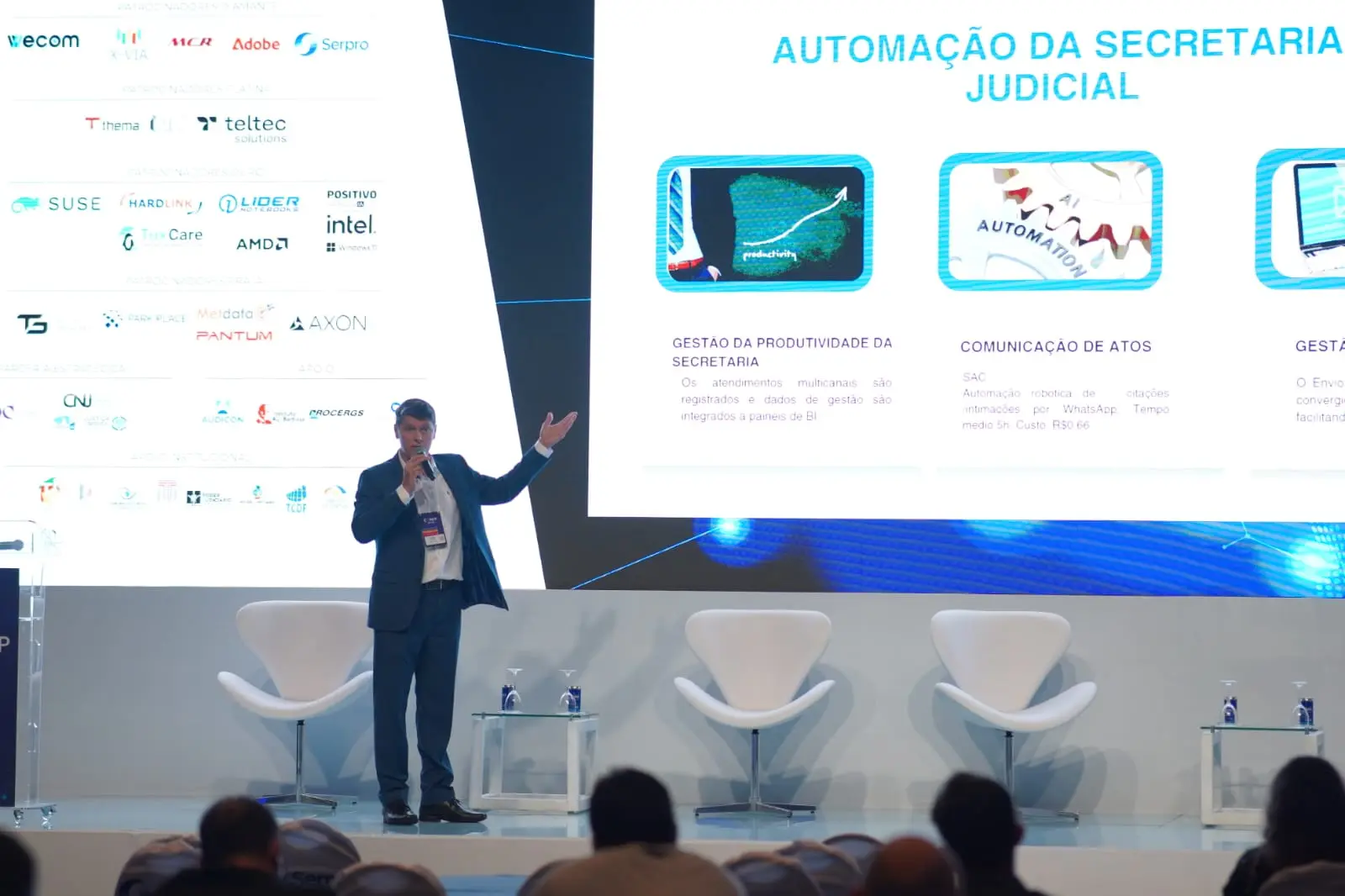 Homem de terno azul, discursa ao microfone no palco do CONIP 2026, com telão exibindo slide sobre "Automação da Secretaria Judicial".