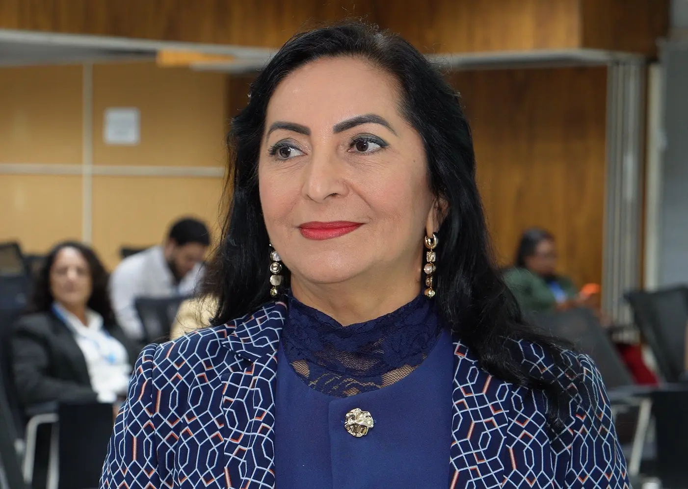 Foto horizontal que mostra a coordenadora de Gestão de Pessoas do TJMT, Claudenice Deijany, do busto pra cima. Ela é uma mulher de pele parda, olhos castanhos, longos cabelos lisos e pretos, usando blusa azul e blazer azul com estampa geométrica em tons de azul e laranjado e brincos pendentes.