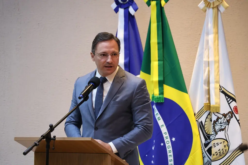Foto horizontal em plano médio que mostra o conselheiro do CNJ, Ulisses Rabaneda, falando ao microfone, na tribuna do plenário do TJMT. Ele é um home branco, de cabelos castanhos, usando camisa branca, gravata azul, terno cinza e óculos de grau. 