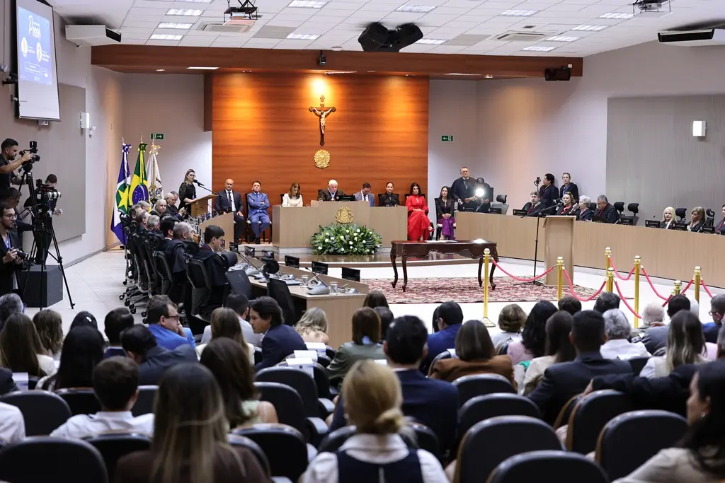 Foto horizontal em plano aberto que mostra o plenário do Tribunal de Justiça cheio de pessoas sentadas na plateia, à frente, os desembargadores sentados em seus lugares e o dispositivo de honra composto ao centro.