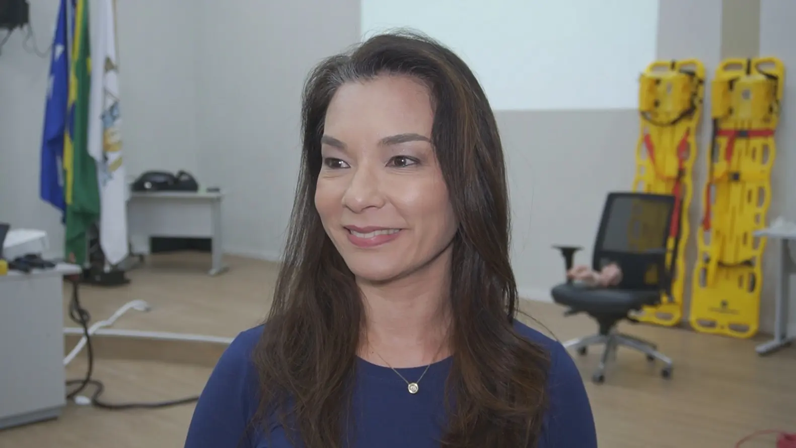 Foto horizontal em plano fechado que mostra a juíza Hannae Yamamura, do busto pra cima, sorrindo. ela é uma mulher branca, com traços orientais, cabelos longos e castanhos, usando blusa azul marinho. 