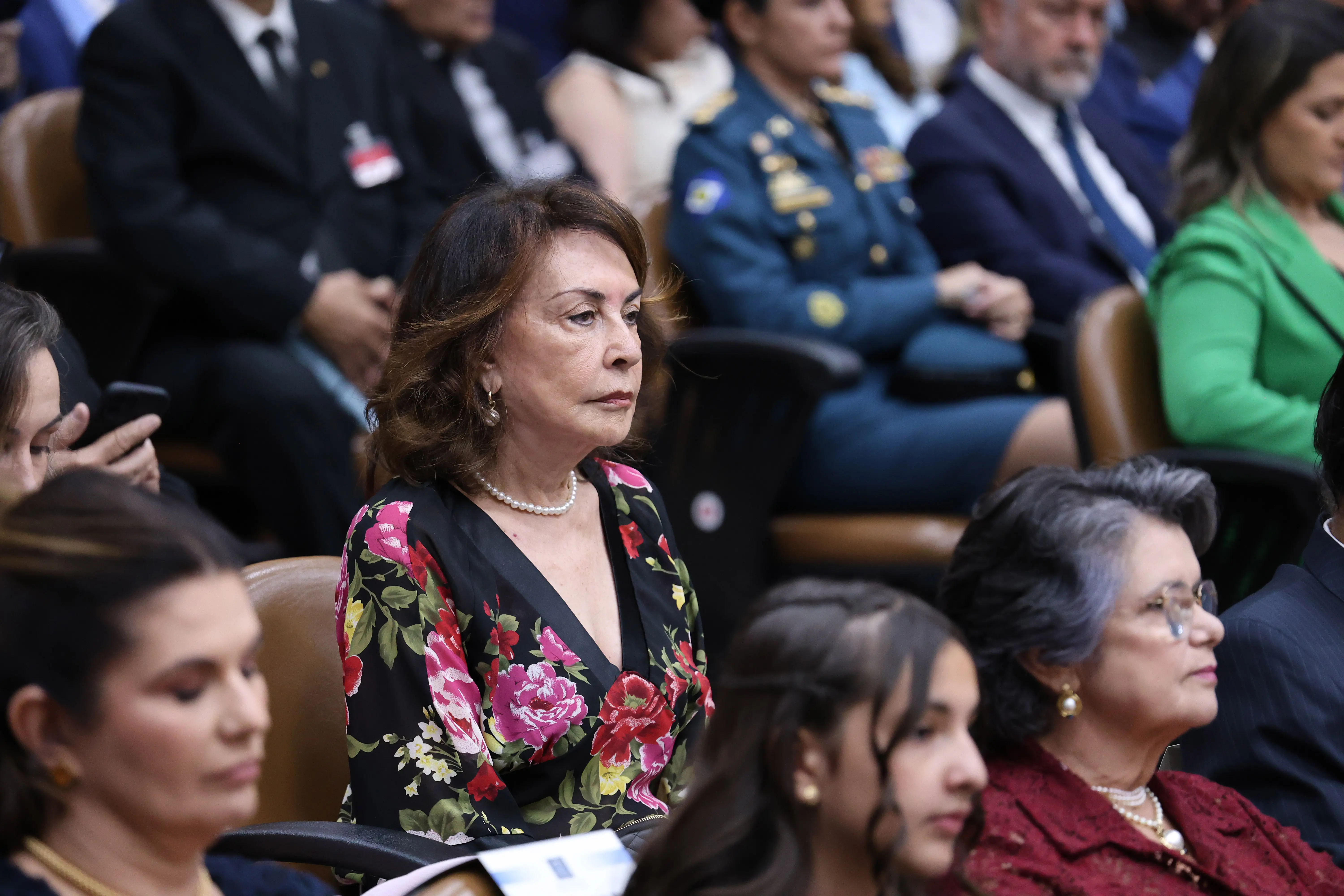 Mãe do desembargador Ricardo Almeida sentada na plateia do Plenário do TJMT. Ela é uma senhora branca, magra, de cabelos castanhos, usando camisa preta com estampa de rosas.