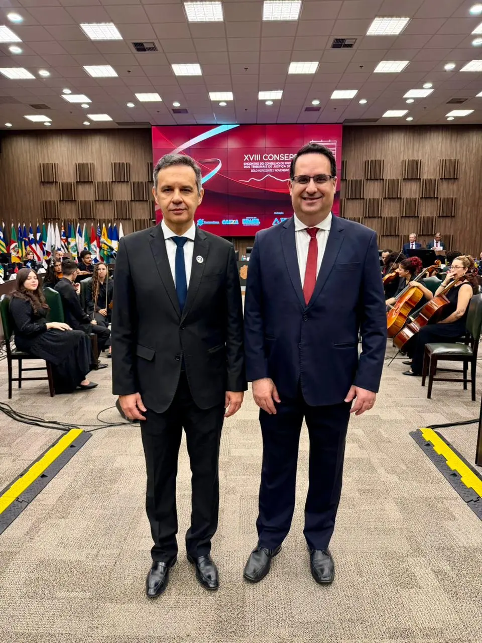 Juízes auxiliares da Presidência do TJMT, Agamenon Alcântara e Túlio Duailibi posam para foto em pé, sorrindo, no Plenário do TJMG. Eles são homens brancos, usando roupa social (terno e gravata).