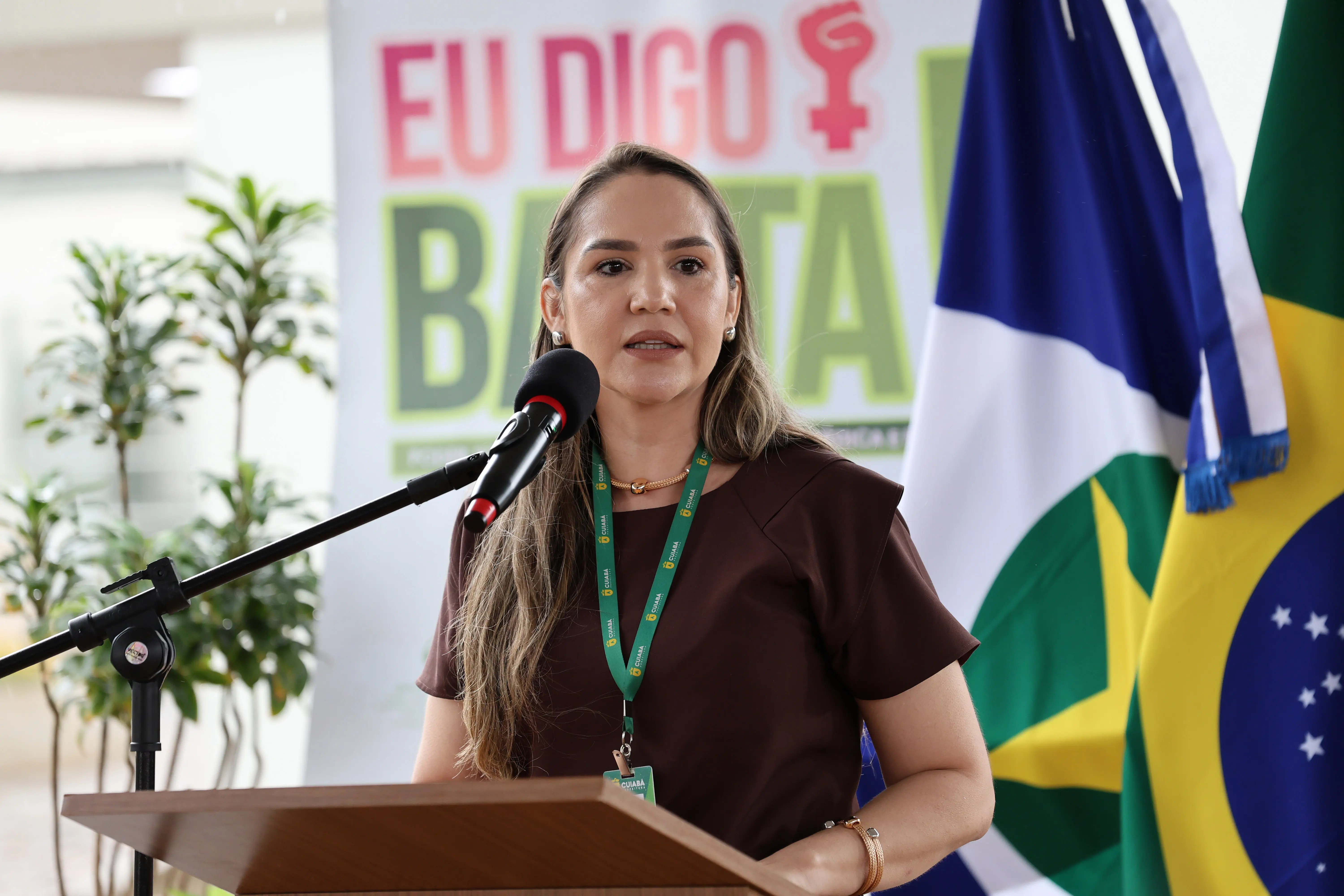 Hadassah Suzannah, mulher de pele clara e cabelos longos, fala em púlpito. Veste blusa marrom e usa crachá com cordão verde. Ao fundo, banner 