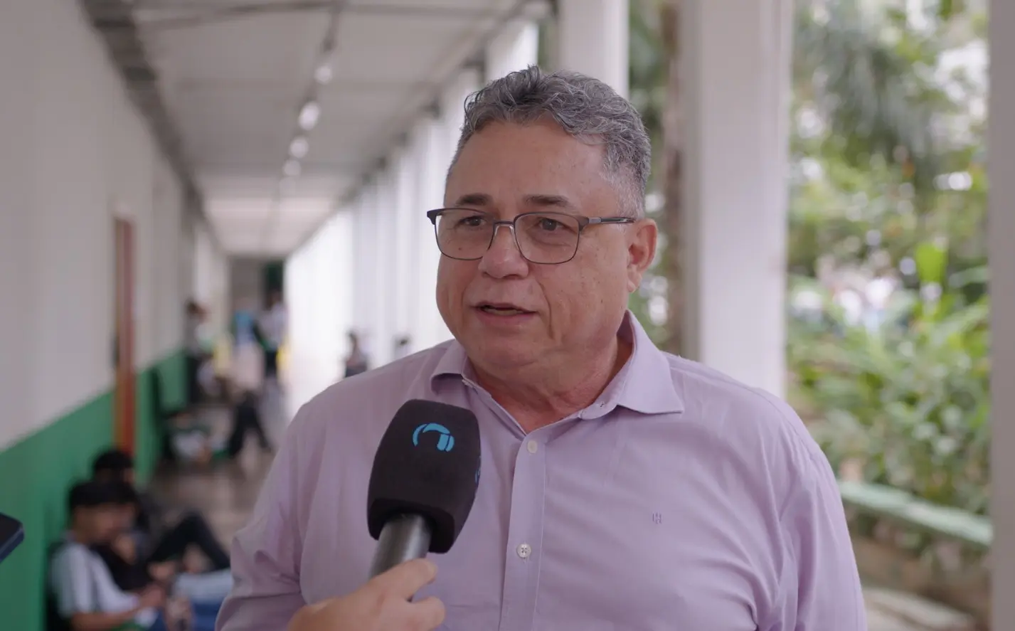 Foto horizontal em plano médio que mostra o diretor-geral do IFMT campus Octayde Jorge da Silva, Alceu Cardoso, durante entrevista à TV Justiça, no corredor da escola. Ele é um senhor de pele clara, cabelo grisalho, usando camisa social lilás e óculos de grau.