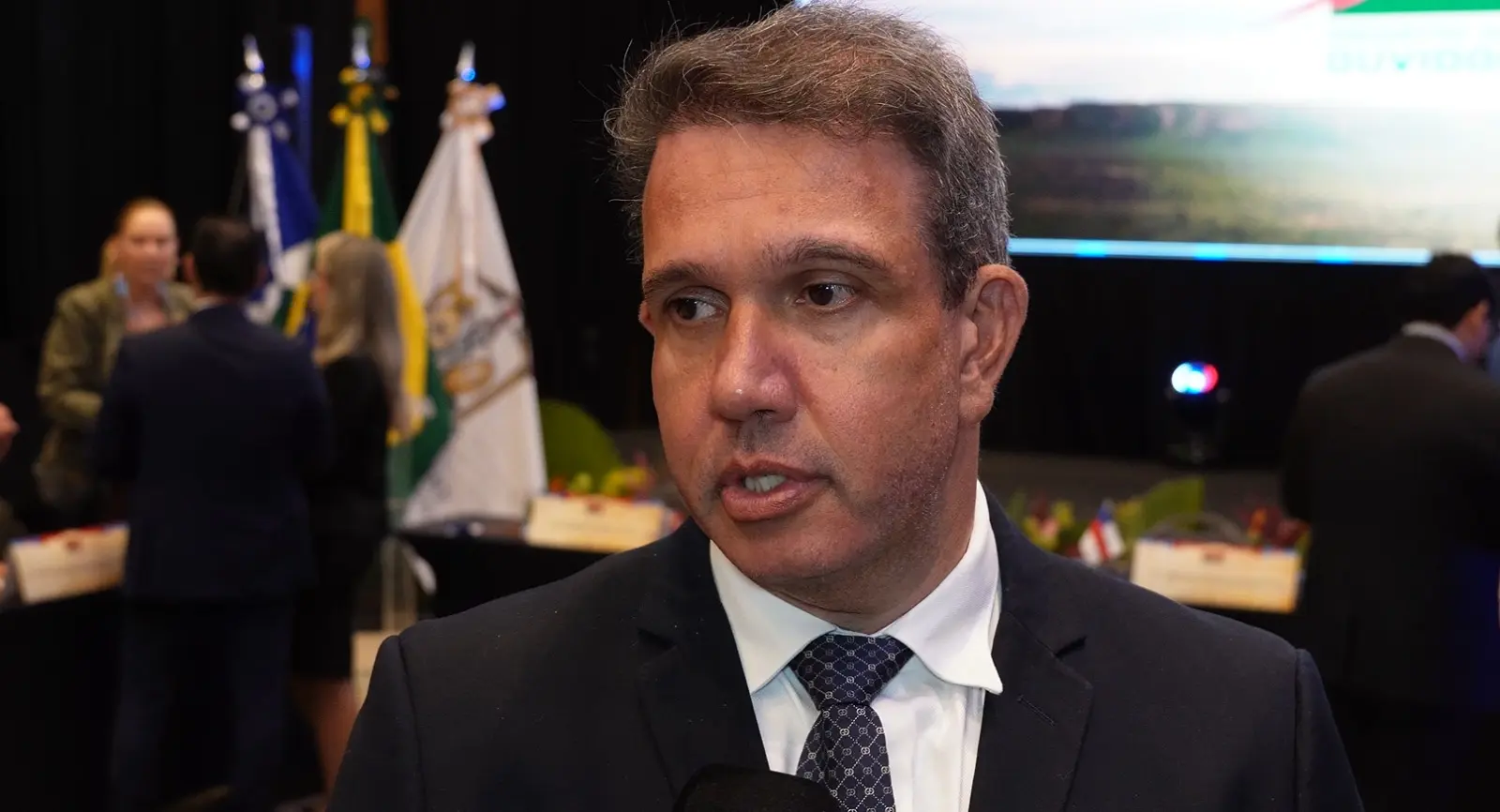 Foto horizontal em plano fechado que mostra o desembargador Luiz Octávio Saboia durante entrevista à TV Justiça. ele é um homem branco, de olhos castanhos e cabelos grisalhos, usando camisa branca, terno preto e gravata azul marinho estampada.