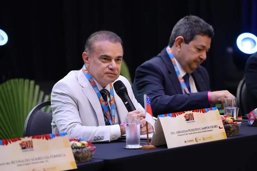 Foto horizontal do ouvidor-geral do Poder Judiciário do Amazonas e presidente do Cojud, desembargador Abraham Peixoto Campos Filho, falando ao microfone, no dispositivo de honra do Encontro do Colégio Nacional de Ouvidores Judiciais. ele é um homem branco, usando terno branco.