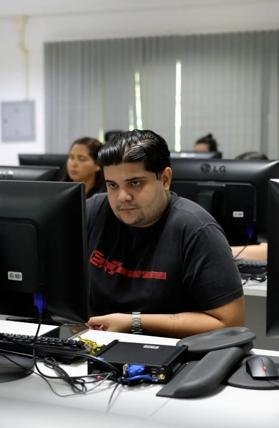 Foto vertical que mostra o estagiário de Contabilidade, Mateus Augusto participando da capacitação no laboratório de computação da Escola dos Servidores. Sentado em frente ao computador, ele acompanha as atividades práticas realizadas durante o curso.